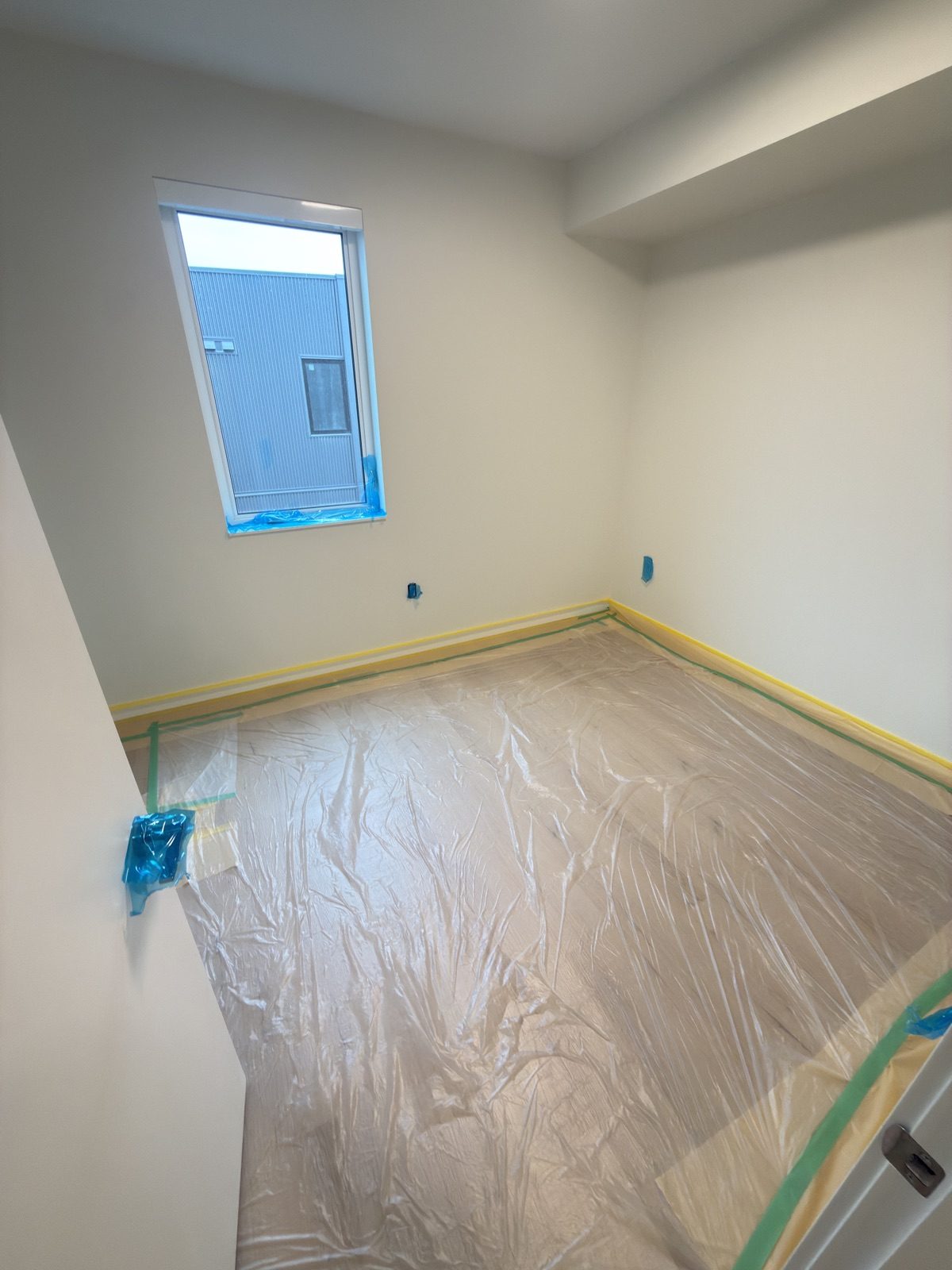 Bedroom floor covered wall to wall in plastic, with outlets and window taped