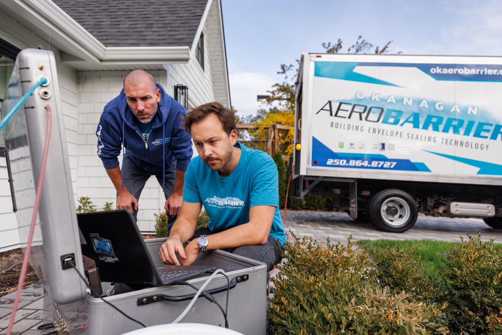 Okanagan AeroBarrier running a seal at a Kelowna home, crew at the blower-door laptop with the branded truck